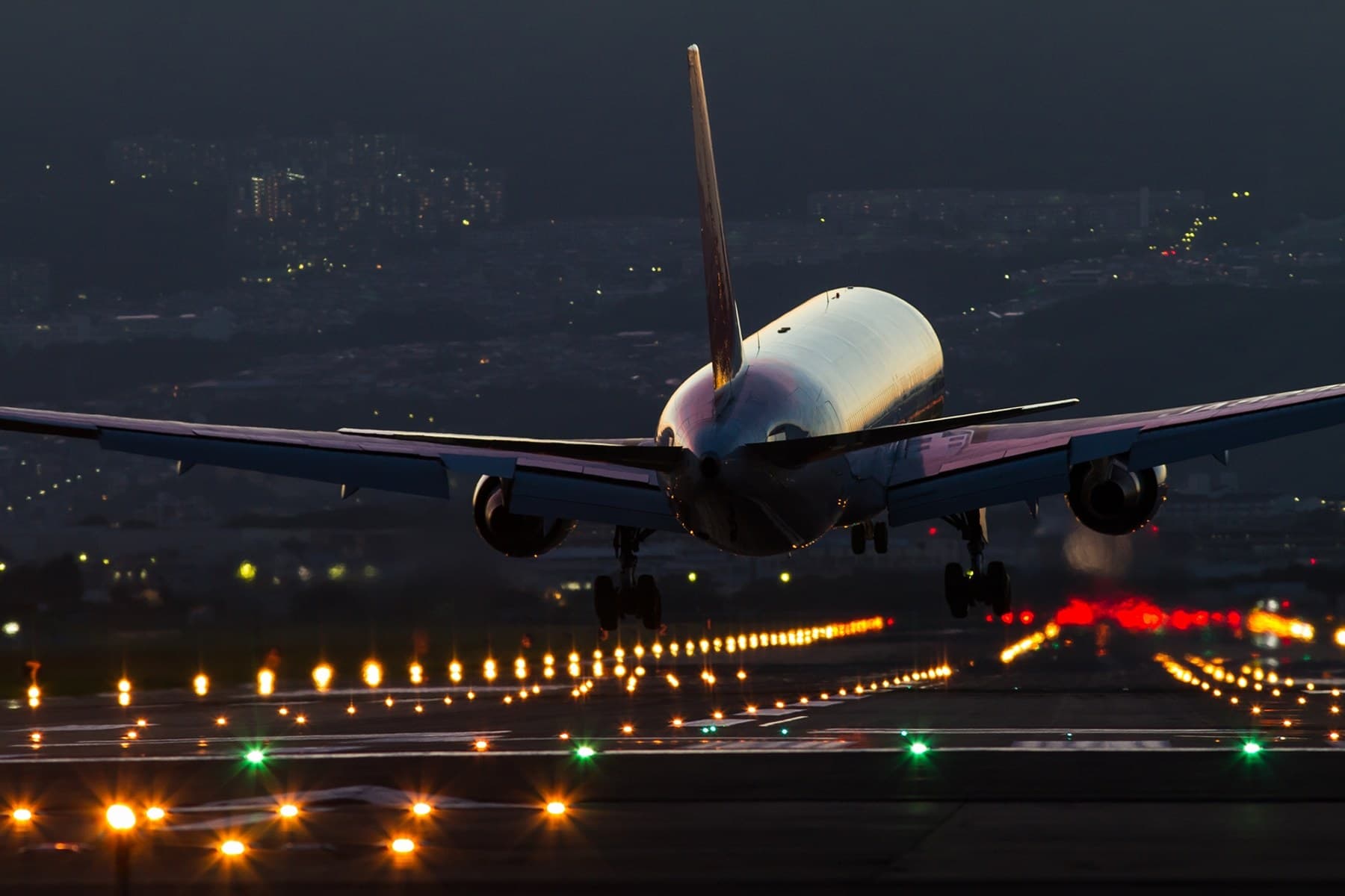 Aviones de pasajeros aterrizando de noche entre aviones y luces de pista en el Aeropuerto Internacional de Osaka